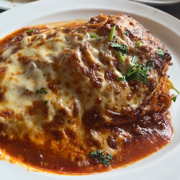Baked spaghetti with melted mozzarella cheese and rich red sauce, garnished with fresh parsley.