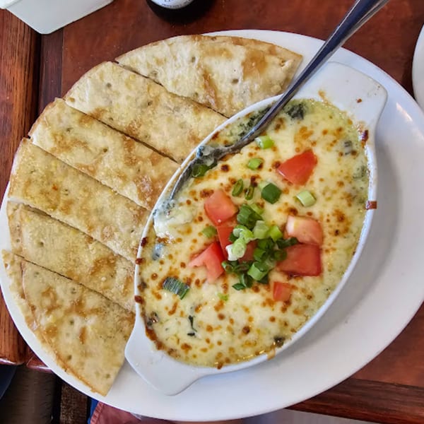 Baked spinach and artichoke dip with melted cheese, diced tomatoes, and green onions, served with flatbread.