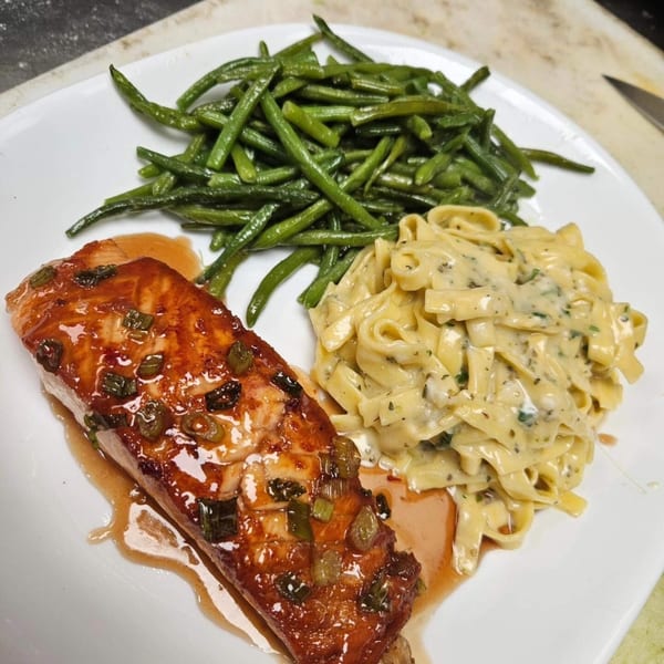 Glazed salmon with green beans and creamy fettuccine pasta on a white plate.