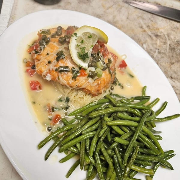 Italian salmon dish with capers, lemon, green beans, and pasta on a white plate.