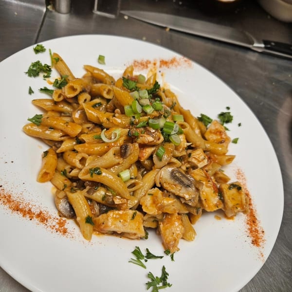 Penne pasta with chicken, mushrooms, and herbs, garnished with paprika and green onions.