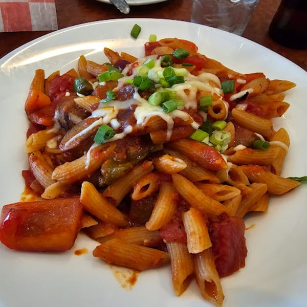 A close-up of Baldo's penne pasta dish with red sauce, melted cheese, and green onions.